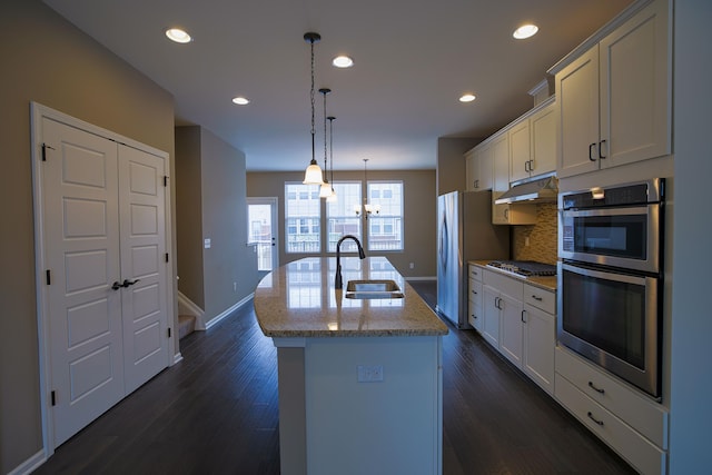 kitchen with sink, hanging light fixtures, light stone counters, an island with sink, and white cabinets