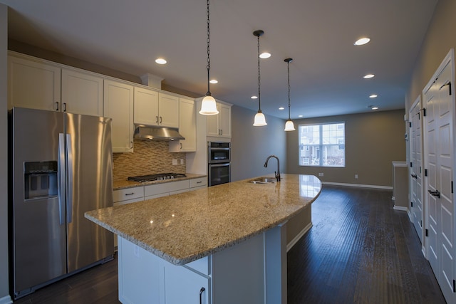 kitchen with appliances with stainless steel finishes, an island with sink, white cabinetry, hanging light fixtures, and light stone counters