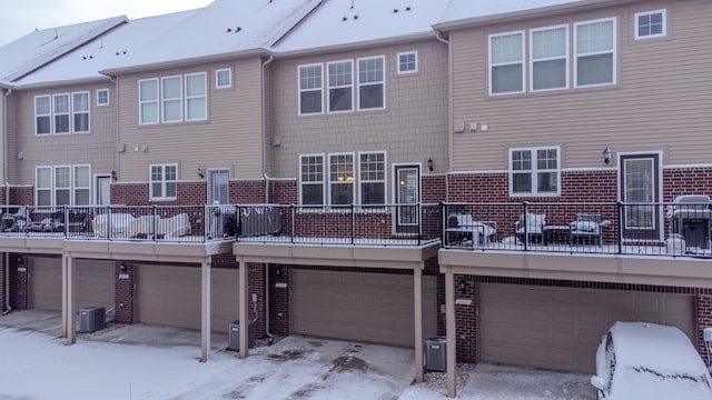 snow covered rear of property with a garage and central AC