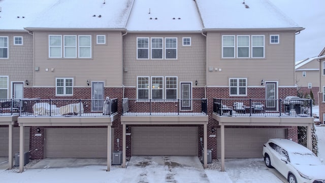 snow covered house featuring a garage and central AC unit