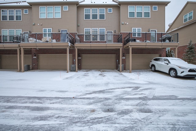 snow covered back of property featuring a garage and central AC