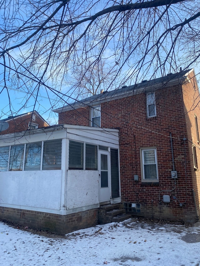 snow covered rear of property with a sunroom