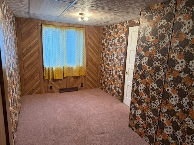 unfurnished room with a drop ceiling, carpet floors, and wooden walls