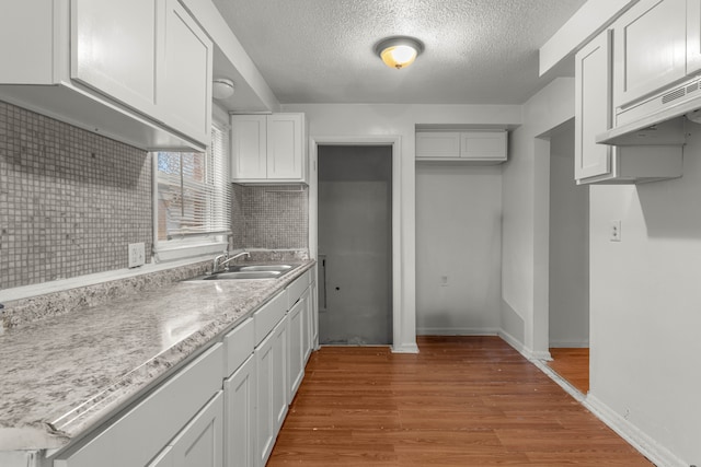 kitchen featuring sink, light hardwood / wood-style floors, white cabinets, a textured ceiling, and decorative backsplash