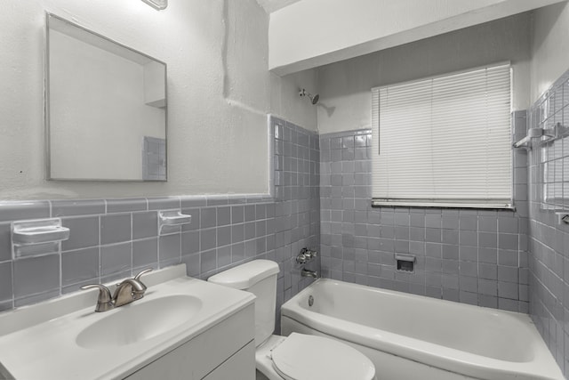 full bathroom featuring tiled shower / bath, vanity, toilet, and tile walls