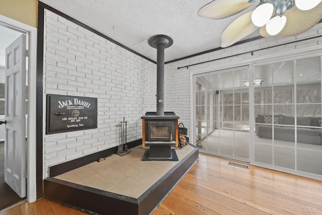 living room featuring brick wall, wood-type flooring, a textured ceiling, and a wood stove