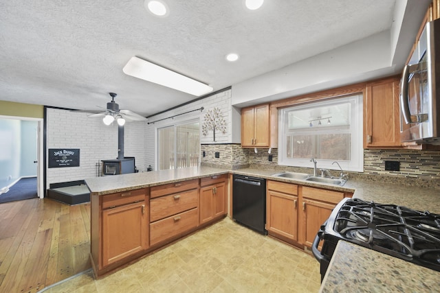 kitchen with sink, black dishwasher, gas stove, kitchen peninsula, and a wood stove