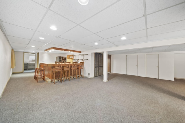 basement with bar, light carpet, and a drop ceiling