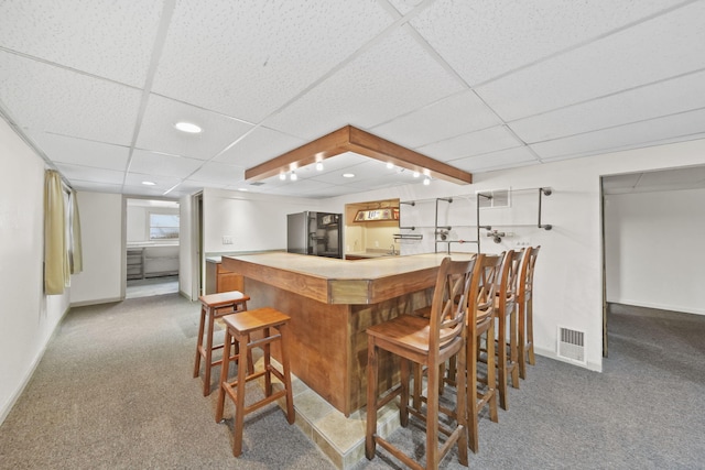 kitchen featuring a paneled ceiling, a kitchen breakfast bar, kitchen peninsula, carpet floors, and white cabinets