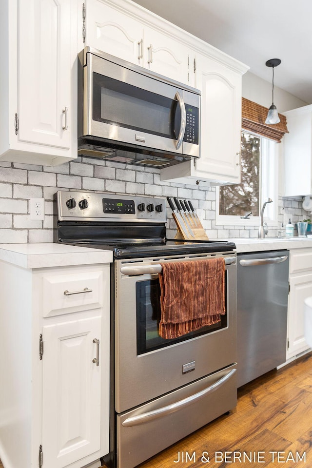 kitchen with white cabinetry, tasteful backsplash, hanging light fixtures, light wood-type flooring, and stainless steel appliances