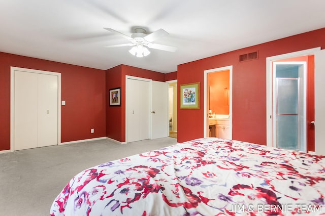 bedroom with ensuite bathroom, two closets, light colored carpet, and ceiling fan