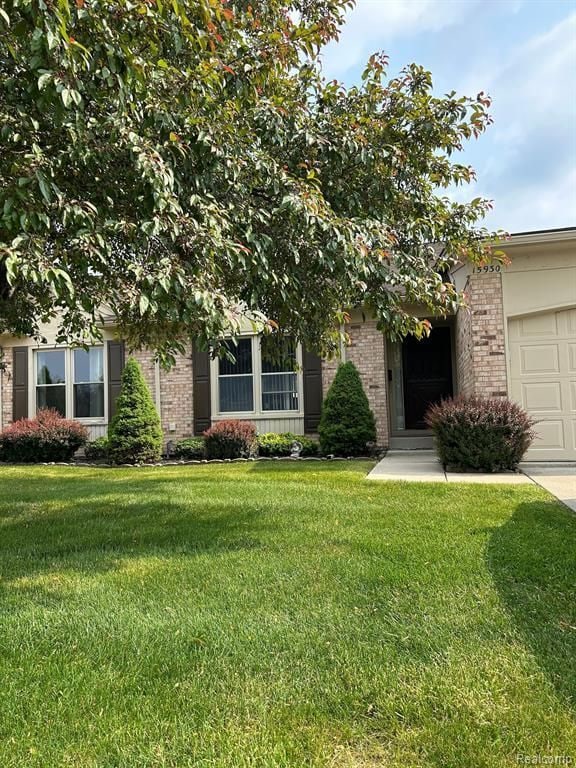 view of property hidden behind natural elements with an attached garage, a front yard, and brick siding