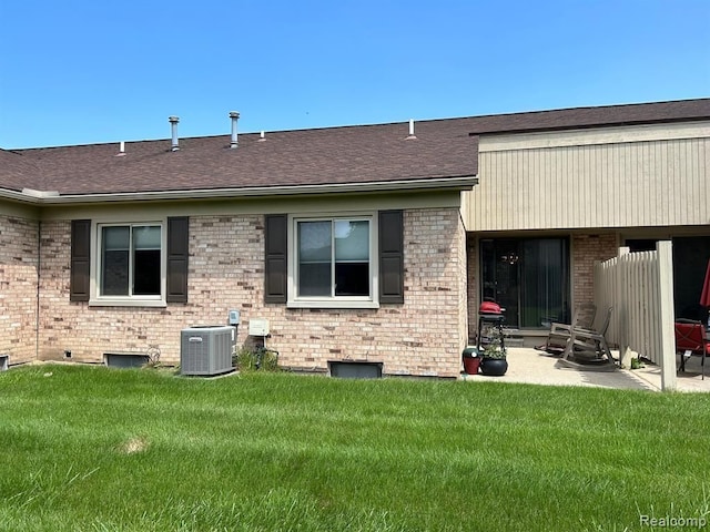 rear view of house featuring brick siding, a yard, a patio, central air condition unit, and a shingled roof