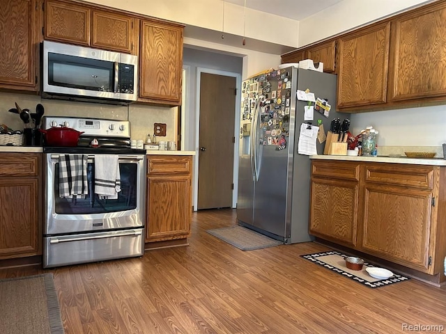 kitchen featuring brown cabinets, stainless steel appliances, light countertops, and wood finished floors