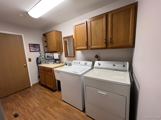 washroom featuring light wood-style floors, cabinet space, a sink, and washer and clothes dryer