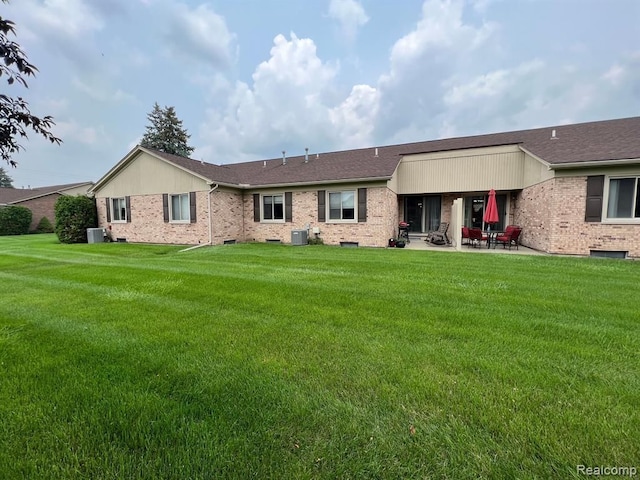 rear view of property with cooling unit, brick siding, and a yard