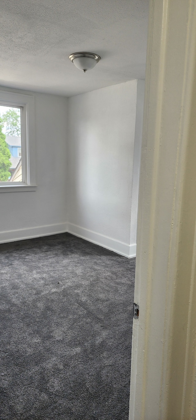 unfurnished room with a textured ceiling and dark colored carpet