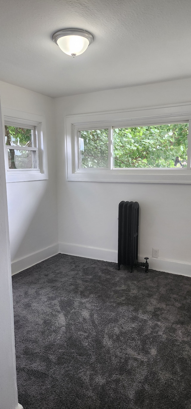 unfurnished room with radiator and dark colored carpet