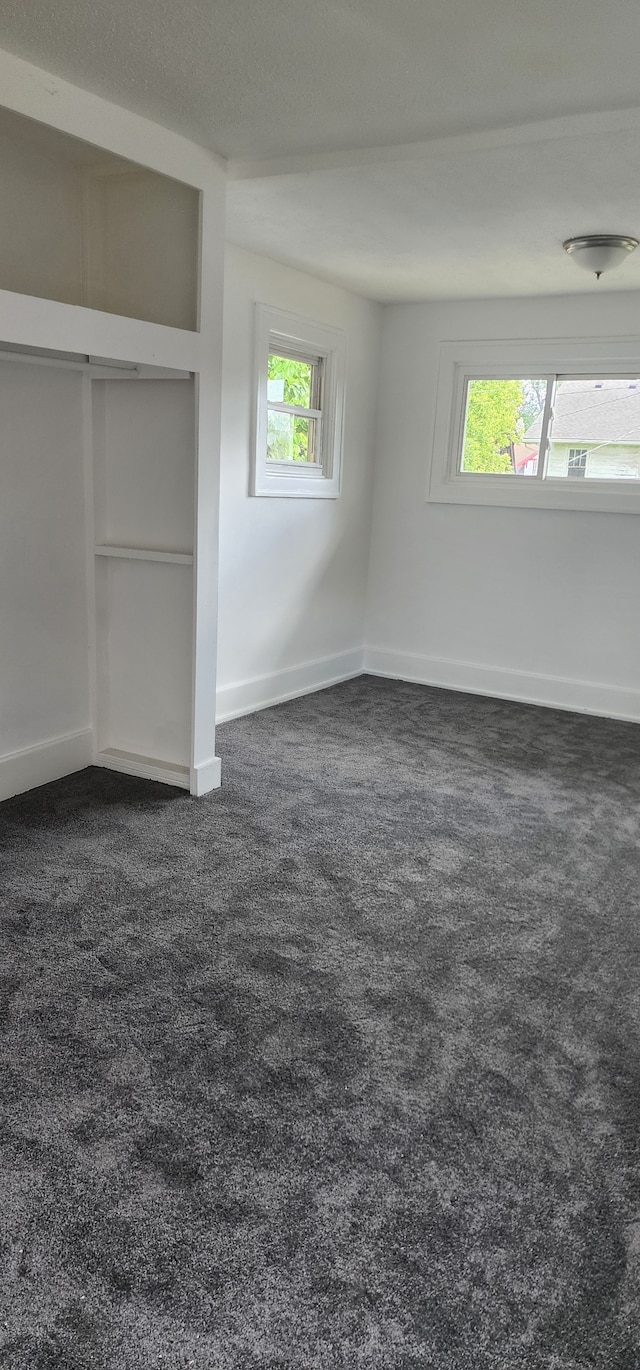 unfurnished bedroom with a closet, dark carpet, and multiple windows