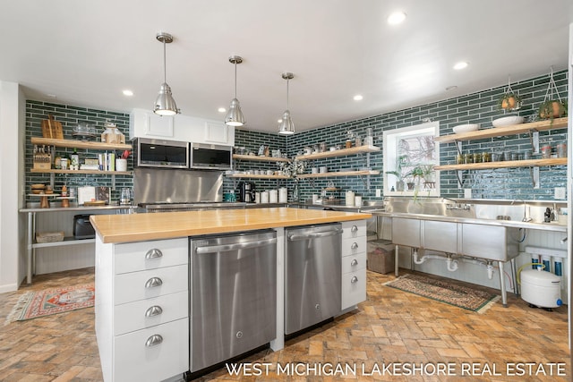 kitchen featuring butcher block countertops, decorative light fixtures, a center island, appliances with stainless steel finishes, and white cabinets