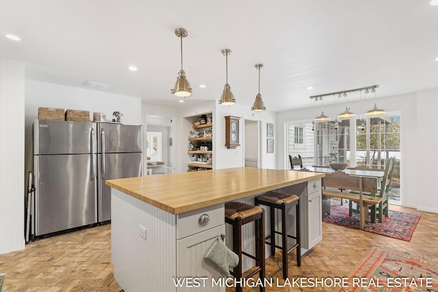 kitchen with a kitchen island, wood counters, pendant lighting, and stainless steel refrigerator