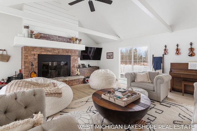 living room with vaulted ceiling with beams, light hardwood / wood-style floors, a brick fireplace, and ceiling fan