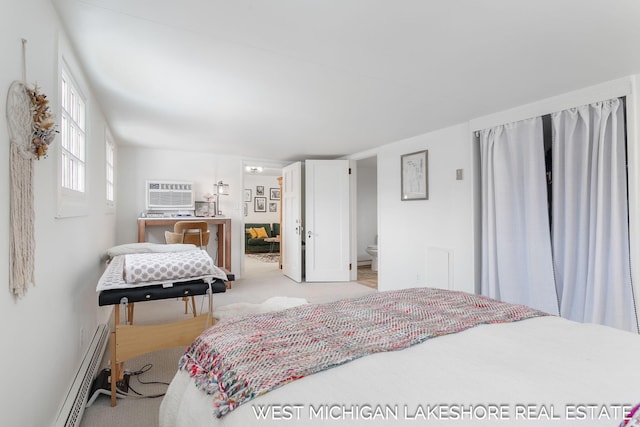 bedroom with baseboard heating, ensuite bath, a wall mounted air conditioner, and light carpet