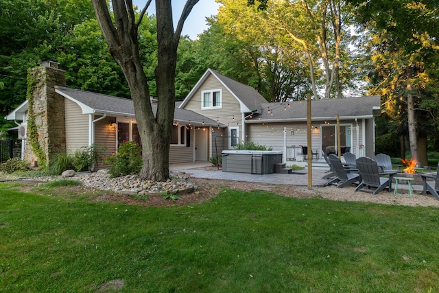 rear view of property featuring a patio, a hot tub, a fire pit, and a lawn