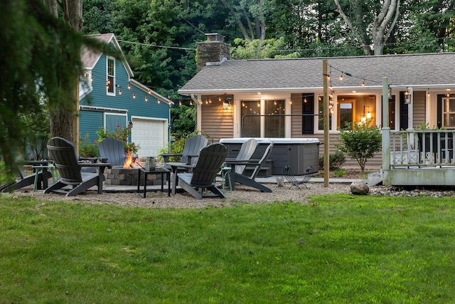 rear view of property featuring a hot tub, a fire pit, and a lawn