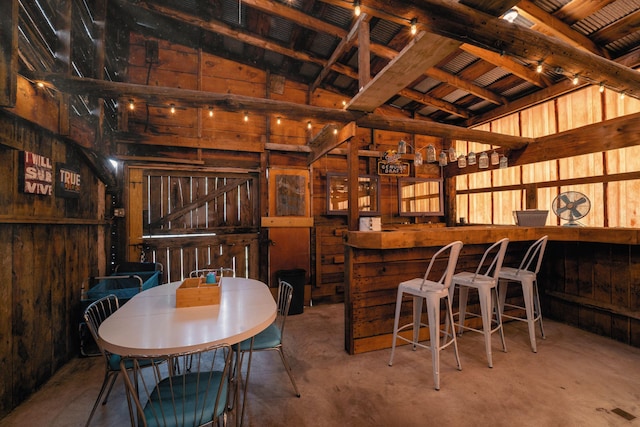 dining space with concrete flooring, beamed ceiling, and wood walls