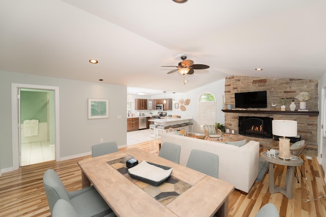 dining space featuring ceiling fan, lofted ceiling, a fireplace, and light hardwood / wood-style floors