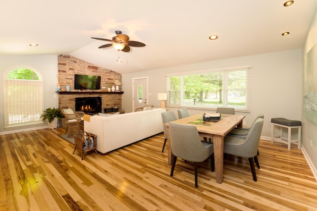 dining room featuring ceiling fan, lofted ceiling, a fireplace, and light hardwood / wood-style floors