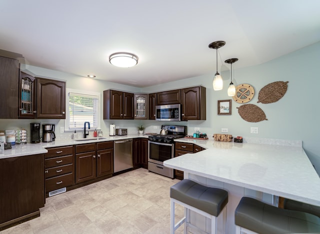 kitchen featuring dark brown cabinetry, sink, hanging light fixtures, appliances with stainless steel finishes, and kitchen peninsula