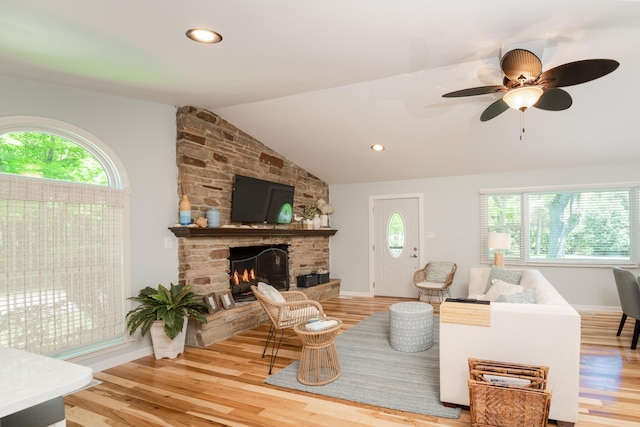 living room with hardwood / wood-style floors, a stone fireplace, vaulted ceiling, and plenty of natural light