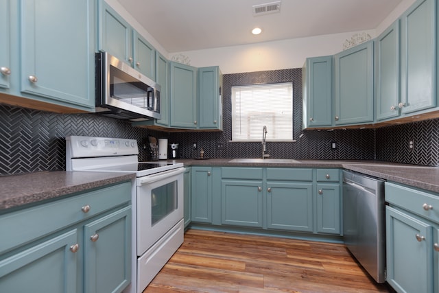 kitchen featuring blue cabinets, sink, decorative backsplash, light hardwood / wood-style floors, and stainless steel appliances