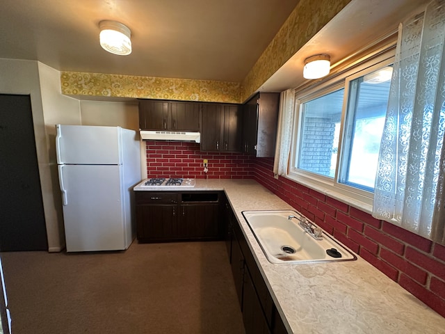 kitchen featuring sink, brick wall, dark brown cabinets, white fridge, and stainless steel gas stovetop