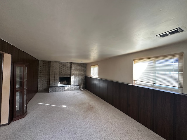 unfurnished living room featuring carpet flooring, a brick fireplace, brick wall, and wood walls