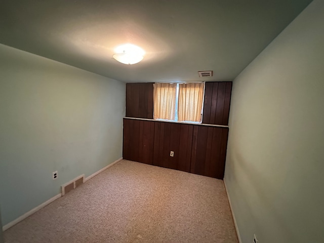 carpeted spare room featuring wooden walls