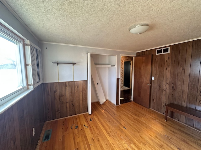 unfurnished bedroom featuring wooden walls, ornamental molding, multiple closets, a textured ceiling, and light wood-type flooring