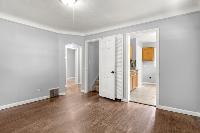 unfurnished bedroom with a textured ceiling, light hardwood / wood-style floors, and ensuite bath