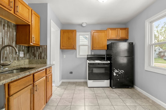 kitchen with sink, white range with gas stovetop, black refrigerator, plenty of natural light, and light stone countertops