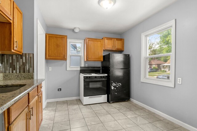 kitchen featuring black refrigerator, range with gas stovetop, tasteful backsplash, sink, and light stone countertops