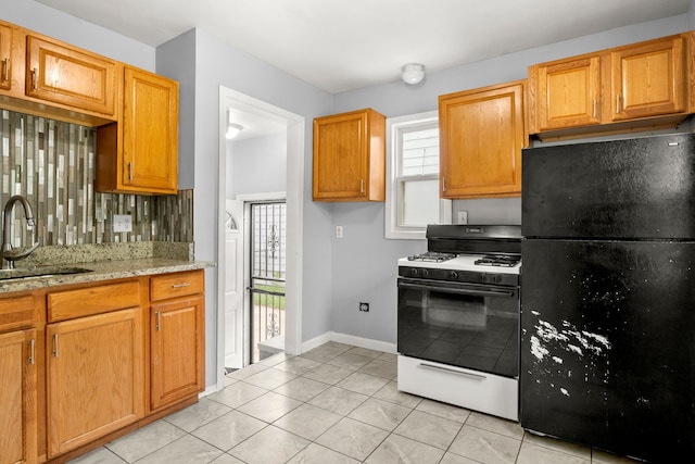 kitchen featuring sink, gas range gas stove, backsplash, light stone counters, and black fridge