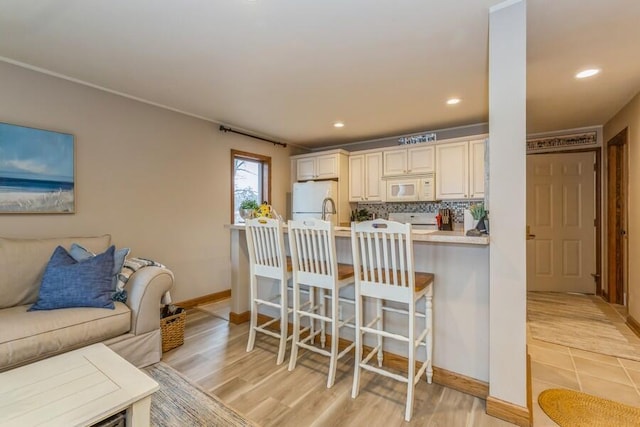 kitchen featuring cream cabinets, a breakfast bar, white appliances, light hardwood / wood-style floors, and decorative backsplash