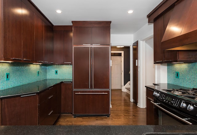 kitchen featuring dark hardwood / wood-style floors, black range oven, dark stone countertops, custom exhaust hood, and paneled built in refrigerator