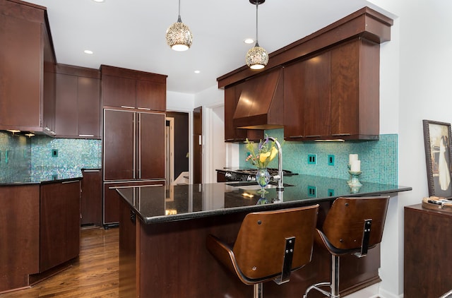 kitchen with a breakfast bar, hanging light fixtures, paneled refrigerator, dark hardwood / wood-style floors, and custom range hood