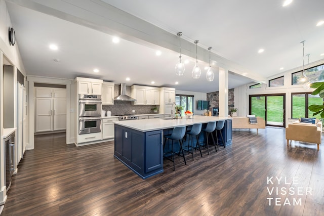 kitchen with pendant lighting, white cabinetry, dark hardwood / wood-style flooring, wall chimney range hood, and a spacious island