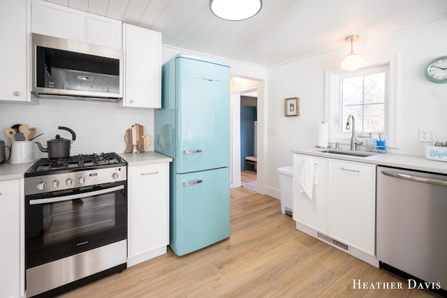 kitchen featuring sink, white cabinetry, hanging light fixtures, stainless steel appliances, and light hardwood / wood-style floors