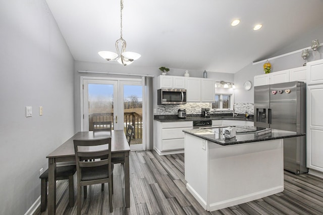 kitchen with vaulted ceiling, a kitchen island, appliances with stainless steel finishes, white cabinets, and backsplash