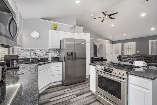 kitchen with sink, vaulted ceiling, appliances with stainless steel finishes, dark stone counters, and white cabinets